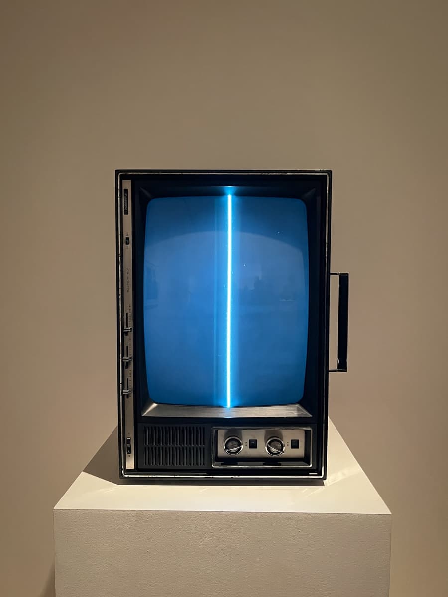 A vintage television placed on a pedestal, its screen displaying a single vertical blue line glowing against a dark background.