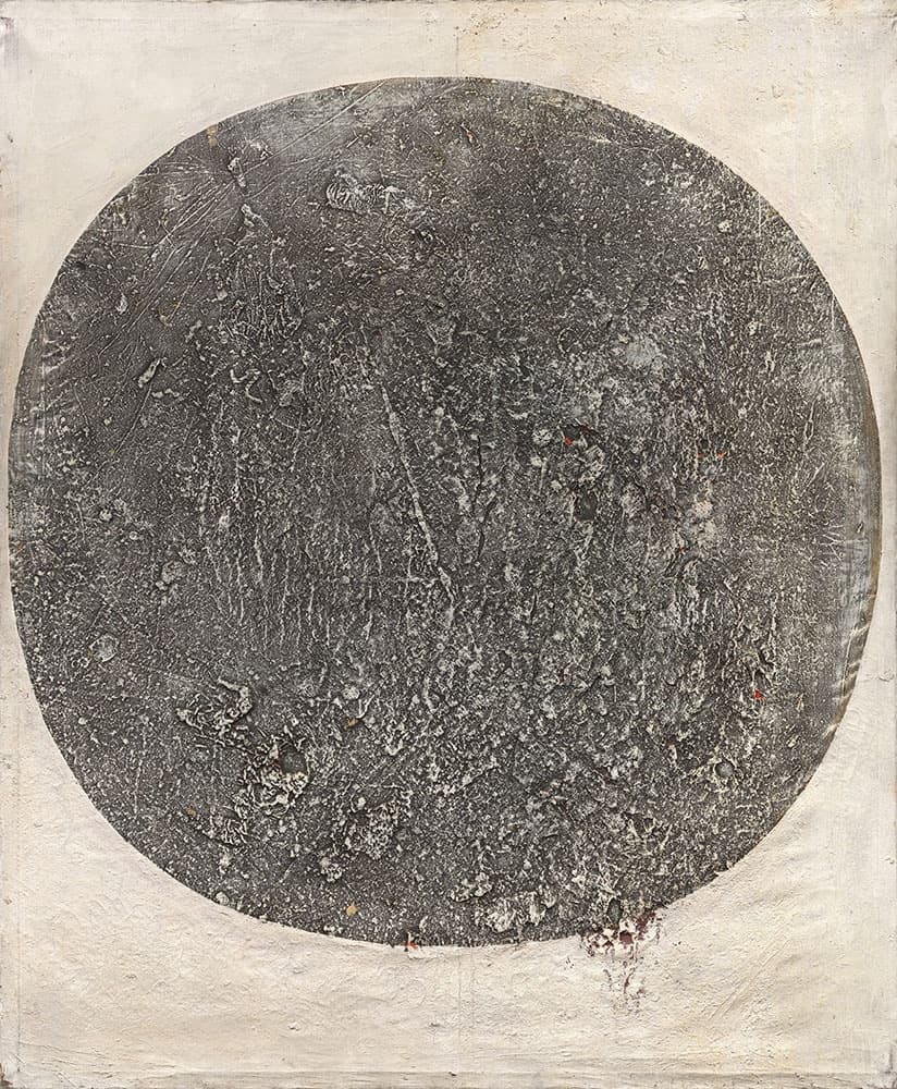 An abstract artwork featuring a rough, circular gray form with a textured surface, displayed on a canvas with off-white corners.