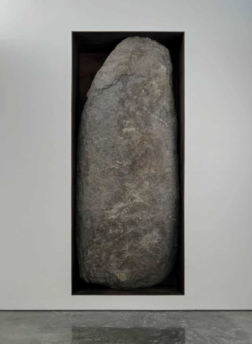 This image captures a large, stone-like object enclosed in a minimalist frame. Its texture and sheer weight contrast with the sleek, clean lines of its enclosure, creating a stark juxtaposition. The monolith evokes a sense of timelessness and permanence, while the modern presentation frame suggests a display of nature or history as art.