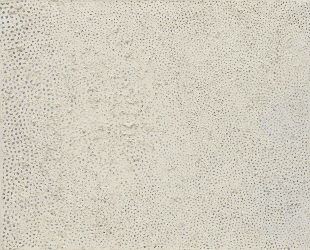 This artwork seems to be a minimalist, textured piece, with small, repetitive patterns creating a tactile surface. The subtle monochromatic palette of whites and grays allows the focus to fall on the material's texture, giving it a quiet, meditative quality.