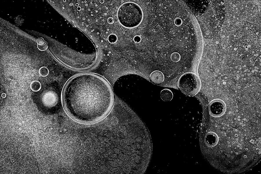 An abstract black-and-white composition featuring circular and bubble-like shapes of various sizes, creating an ethereal, cosmic appearance. The overlapping forms resemble organic patterns or a microscopic view of particles suspended in liquid.
