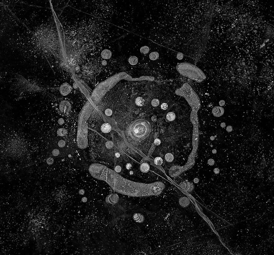 A black-and-white abstract artwork with a central circular formation surrounded by smaller bubble-like shapes and radial streaks, evoking the image of a galaxy or a celestial map. The texture is intricate and suggests a blend of natural and cosmic elements.