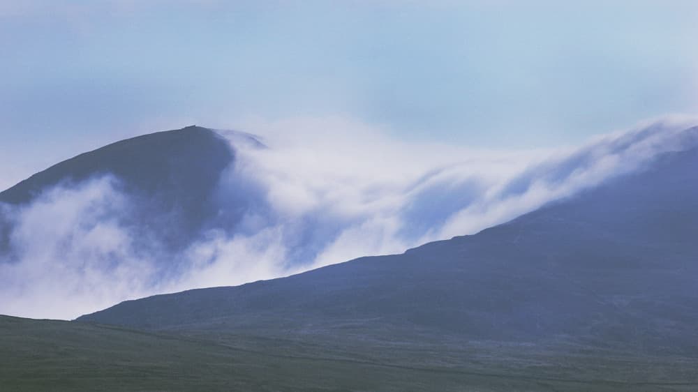 A silhouette of a distant mountain under a deep blue twilight sky, with thick, low-hanging clouds adding a moody, atmospheric tone.