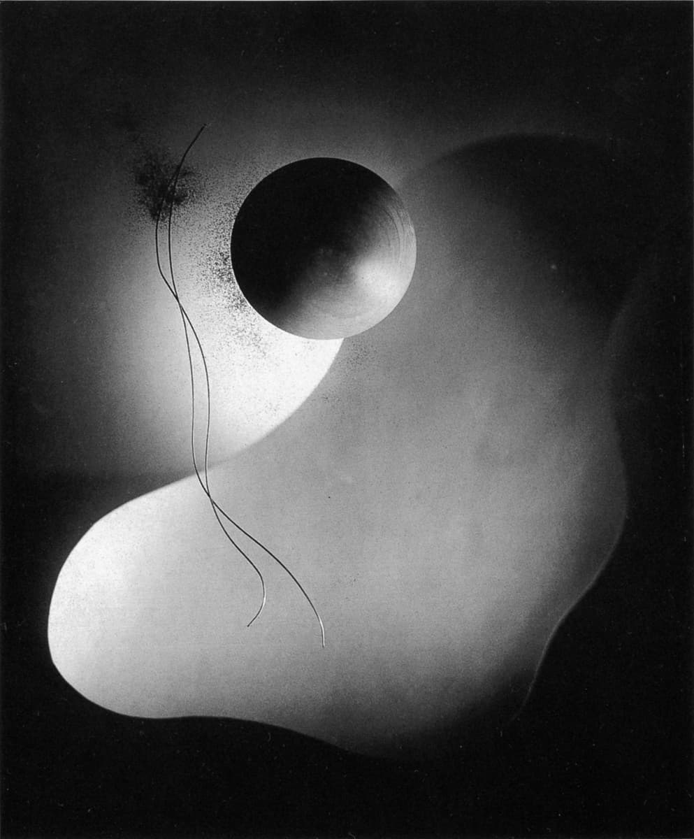 Abstract black-and-white composition featuring a large dark sphere near the center, floating above a softly contoured, organic white shape that fades into a dark background. Two fine, curved lines and a speckled texture emerge near the sphere, adding a sense of motion and ethereality.