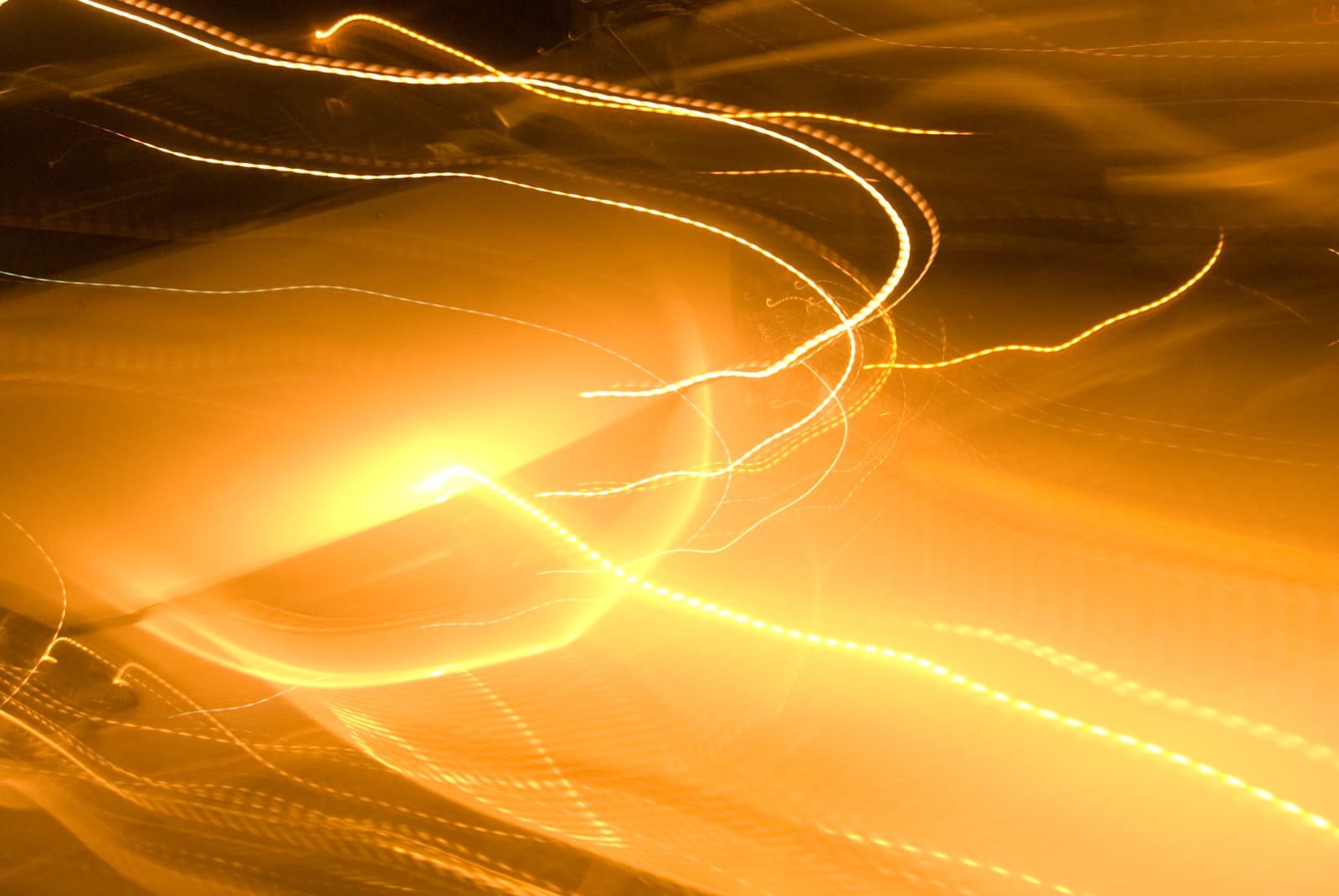 This abstract photograph features streaks of bright golden light swirling across the frame, creating a sense of dynamic movement and energy. The light trails curve and twist in various directions, blending into the warm glow of the background. The fluid lines and vibrant colors evoke a sense of motion, as if the lights are dancing or flowing like waves. The image's blurred and dreamlike quality gives it an otherworldly or surreal atmosphere, emphasizing the ethereal beauty of light in motion.
