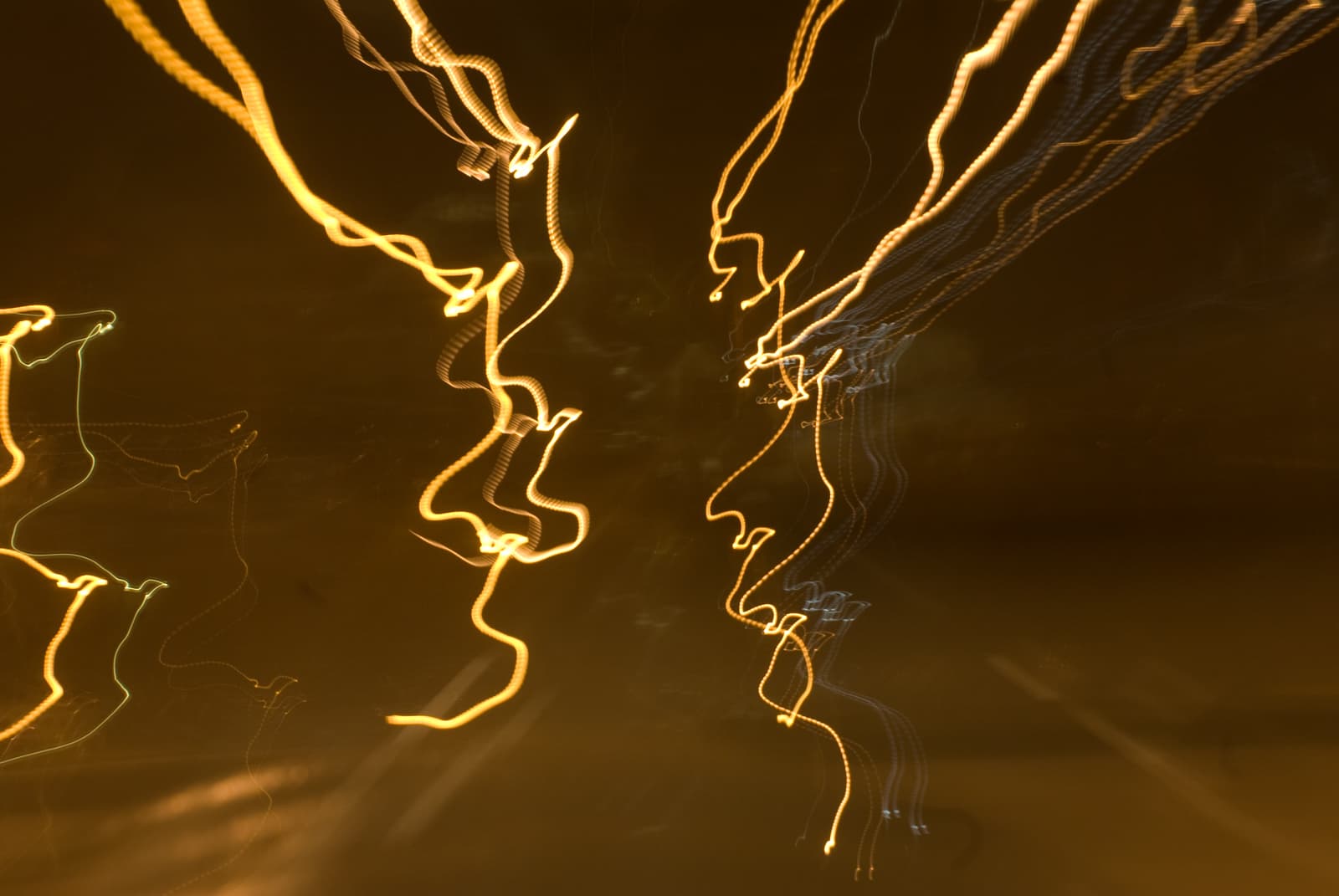 This abstract photograph showcases jagged, swirling streaks of yellow, orange, and white light against a dark background. The light trails seem to twist and dance across the frame, forming chaotic, erratic patterns that suggest movement and energy. The overall effect is dynamic and mesmerizing, with the flowing, wave-like lines creating a sense of spontaneity and unpredictability. The dark backdrop contrasts sharply with the glowing light, making the streaks stand out prominently, while their irregular shapes add to the abstract, dreamlike quality of the image.