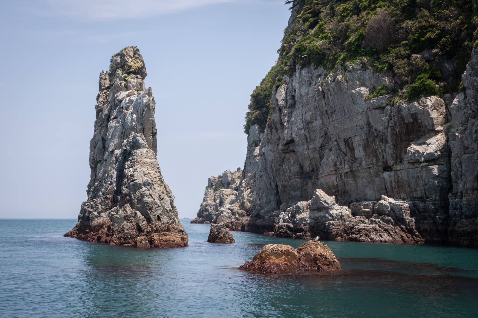 Tall, jagged rock formations rising out of the calm ocean waters, surrounded by smaller rocks and cliffs.
