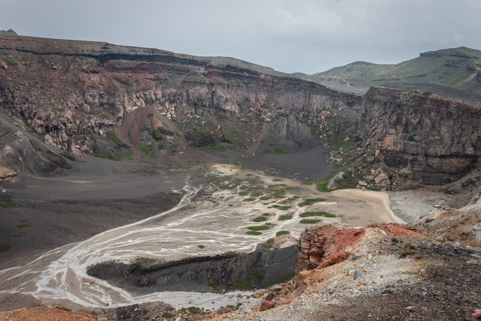 The bottom of a volcanic crater with blackened earth and streaks of white mineral deposits cutting through the rocky basin.