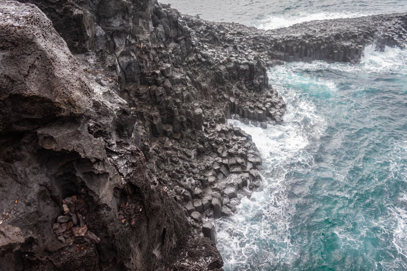 A dramatic view of a rugged volcanic coastline with jagged rocks and crashing ocean waves.