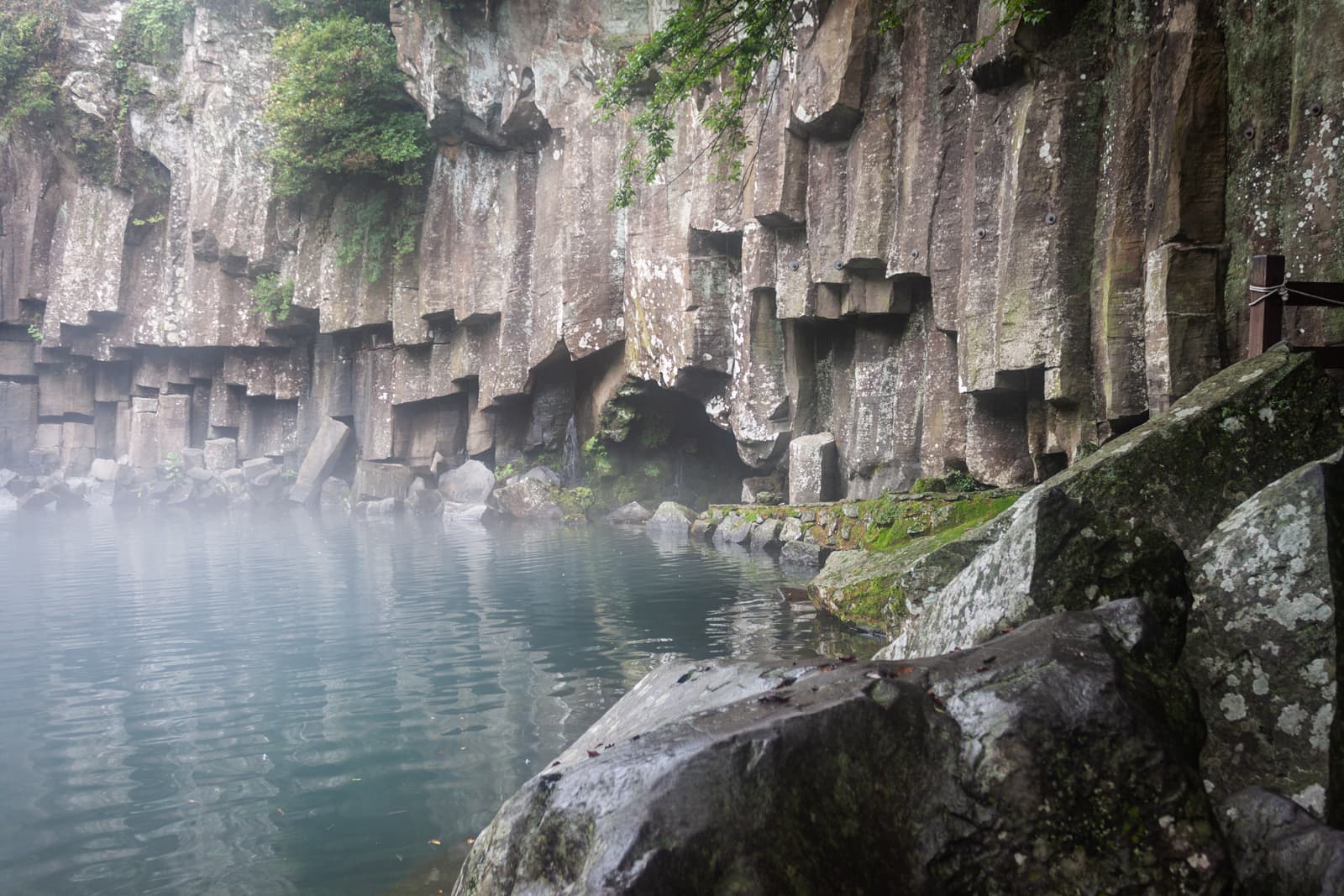 Natural basalt rock formations rise from the edge of a mist-covered lake, creating a serene, ancient atmosphere.