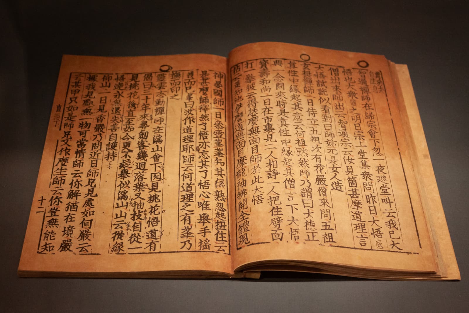 A close-up shot of an open ancient manuscript written in an East Asian script, featuring vertical lines of characters on aged, yellowed paper. The text is neatly aligned, giving an impression of careful preservation.
