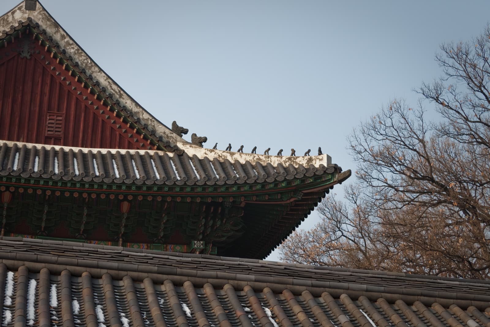 The peak of a temple rooftop adorned with small decorative sculptures of animals and figures, with bare trees in the background and a clear winter sky above.