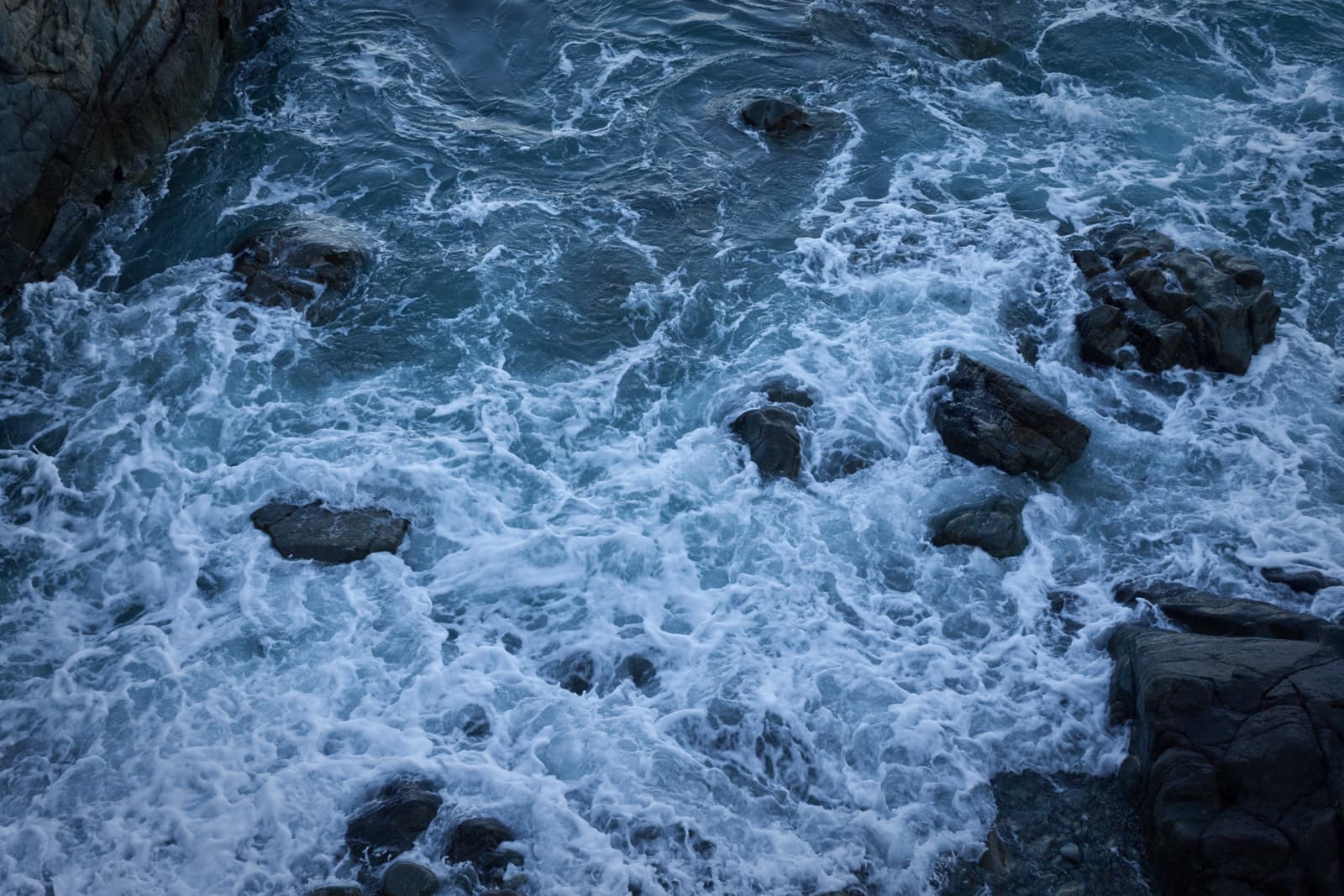 Waves crashing against rocks in a turbulent sea, with white foam contrasting against the dark stones.