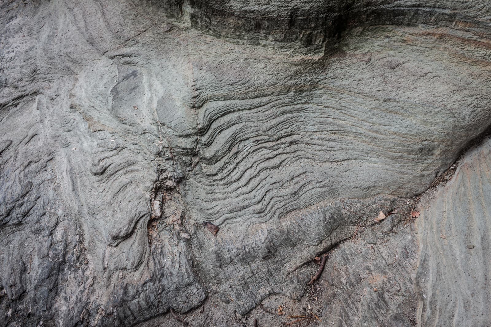 A weathered rock surface with intricate wave-like patterns, possibly caused by years of natural erosion. The rock has a smooth but undulating texture, emphasizing the natural geological formations.