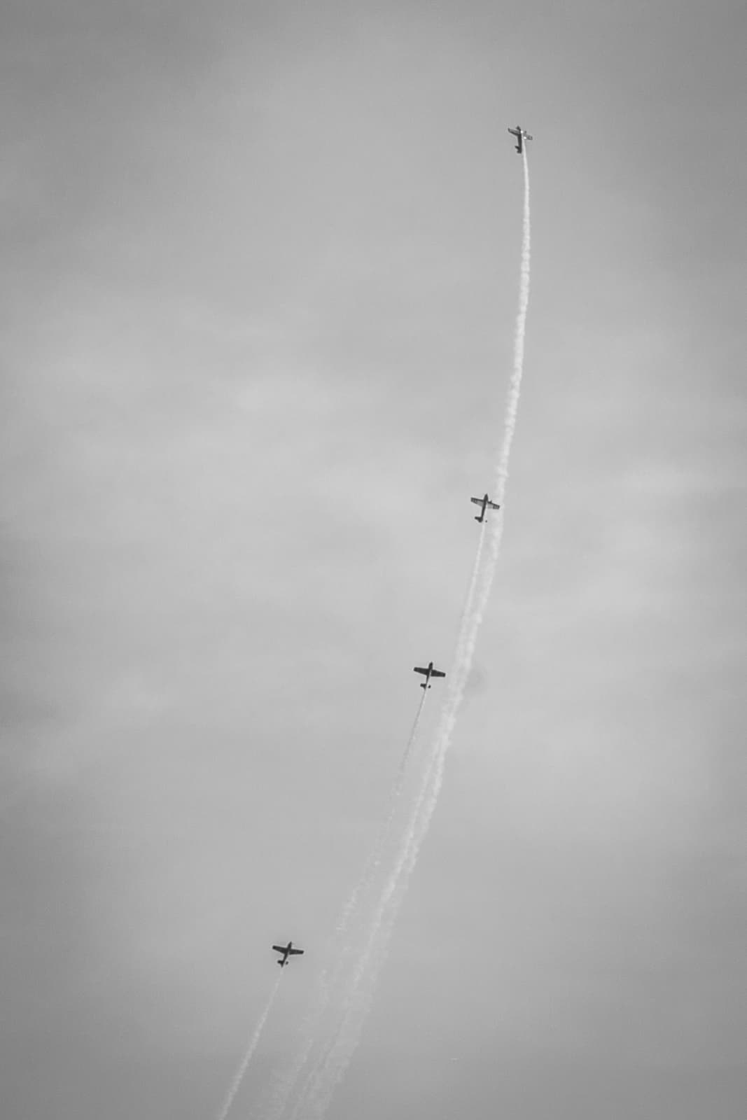 Four airplanes ascending vertically in a staggered line, leaving smoke trails behind them, in a black-and-white image.
