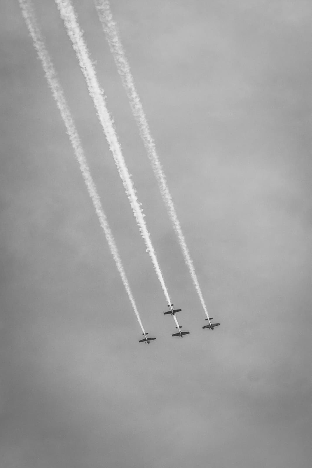 Four airplanes flying in close formation, leaving parallel smoke trails, photographed in black and white.