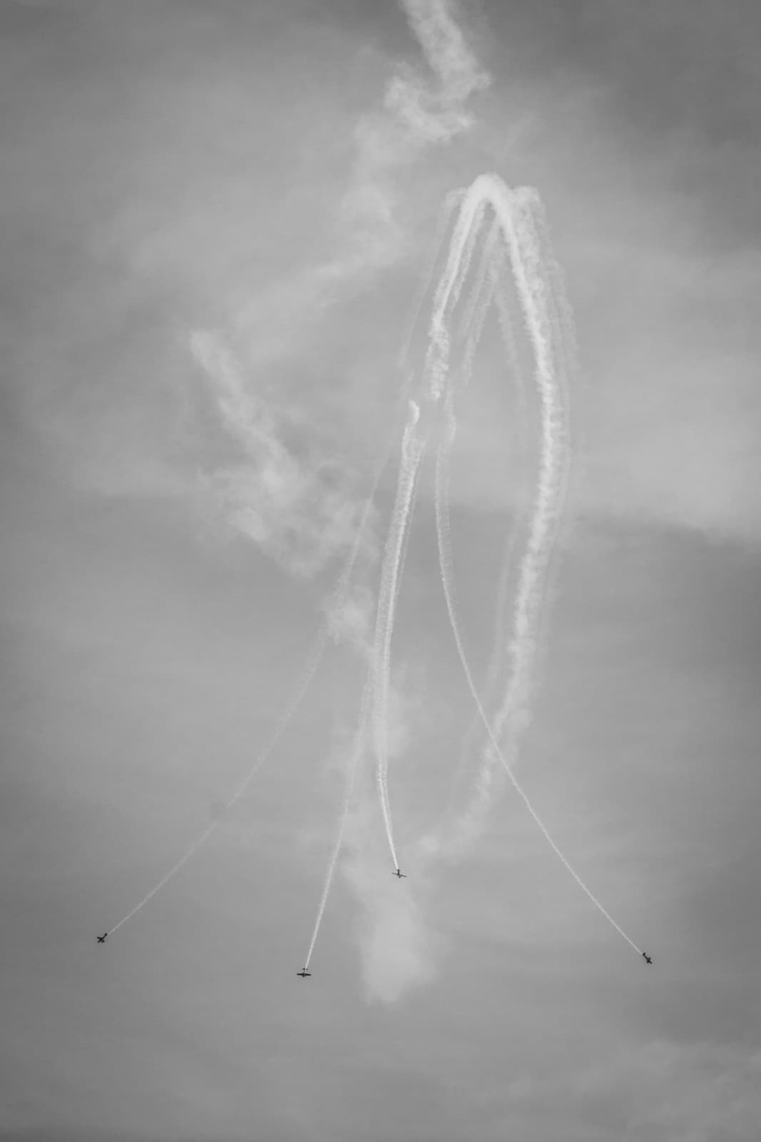 Four airplanes flying upwards with trails of smoke forming a loop, captured in black and white.