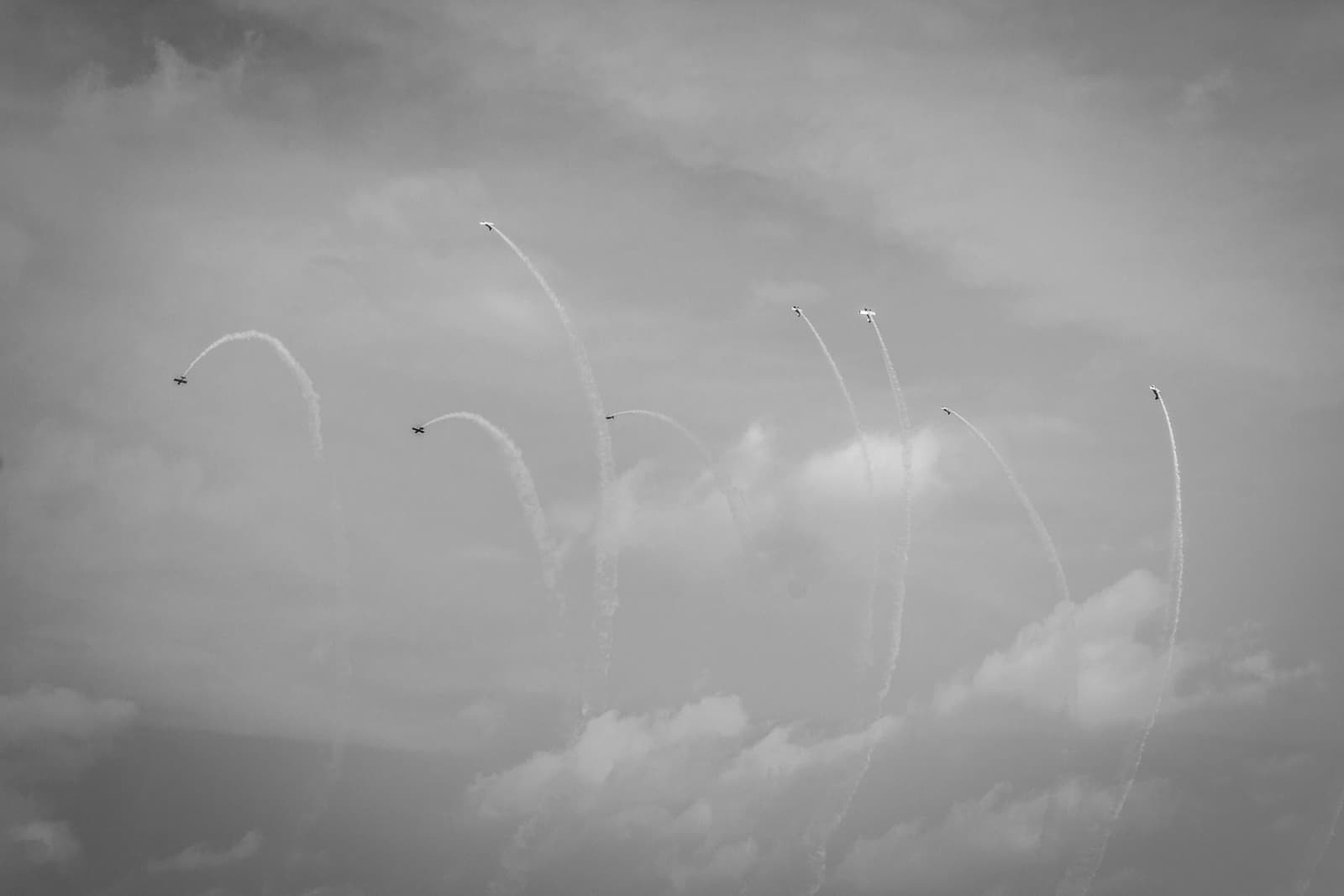 Eight airplanes dispersing in various directions, each leaving a distinct smoke trail against the sky, captured in black and white.