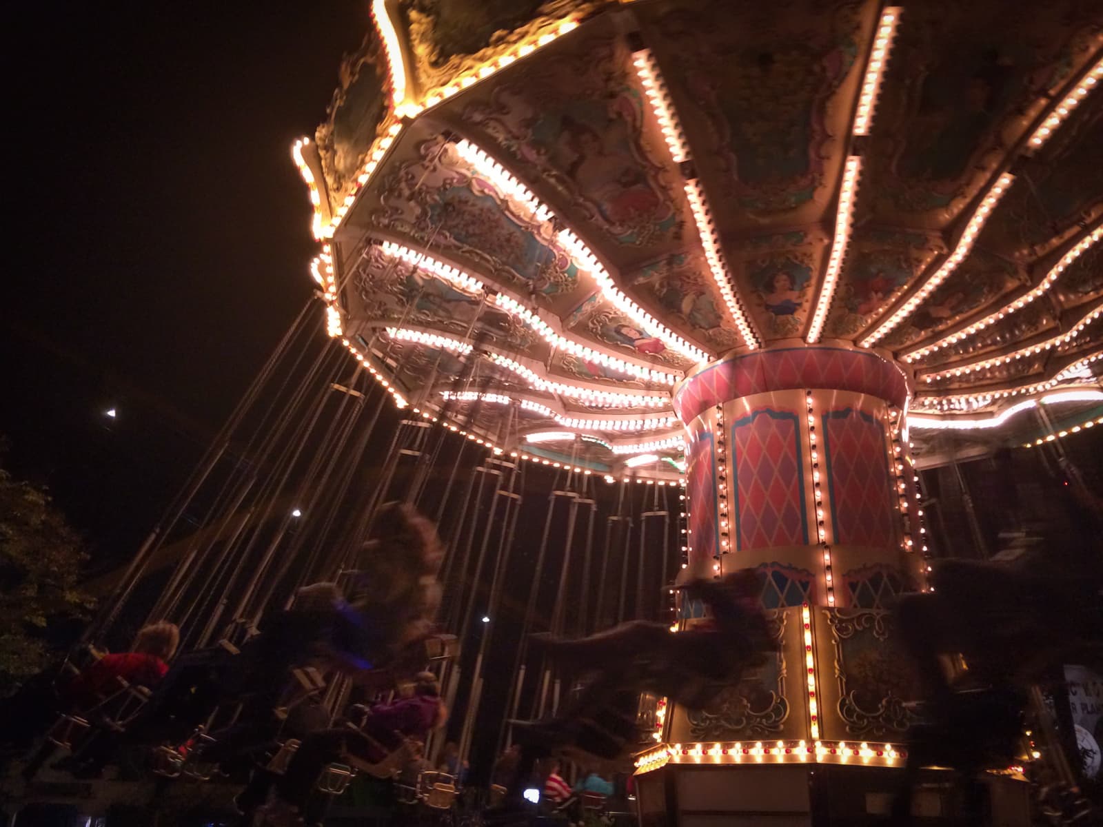A brightly lit swing ride at night with blurred motion from riders swinging in the air, set against a dark sky.