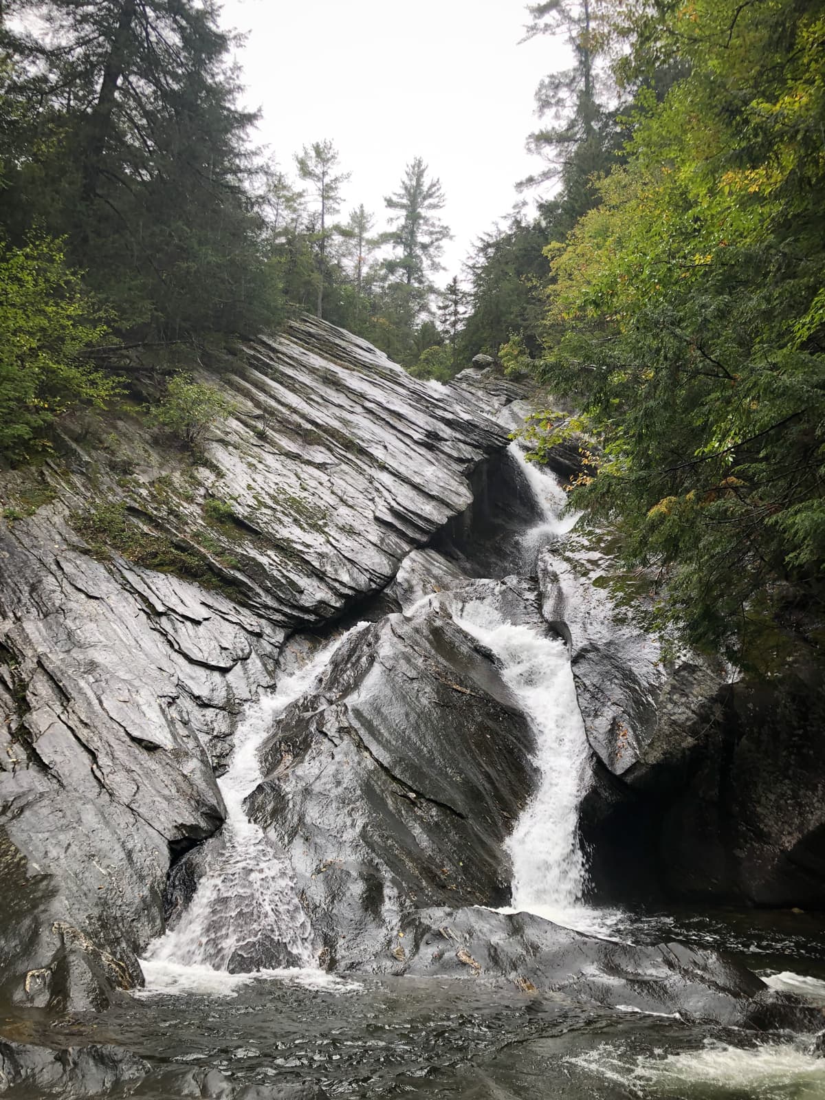 A cascading waterfall flowing down large, angled rock formations in a forest.