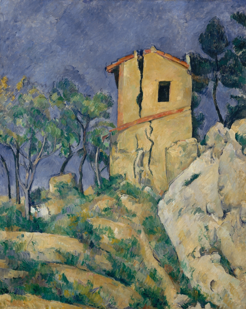 An oil painting depicting a crumbling yellow ochre house with a red-tiled roof, bisected by a dramatic vertical crack running the full height of the facade. The building sits among rocky terrain with scrubby green vegetation and is flanked by tall pine trees. The sky is rendered in broken strokes of lavender and blue-gray. The blocky, faceted treatment of rock and foliage is characteristic of Cézanne's mature style.