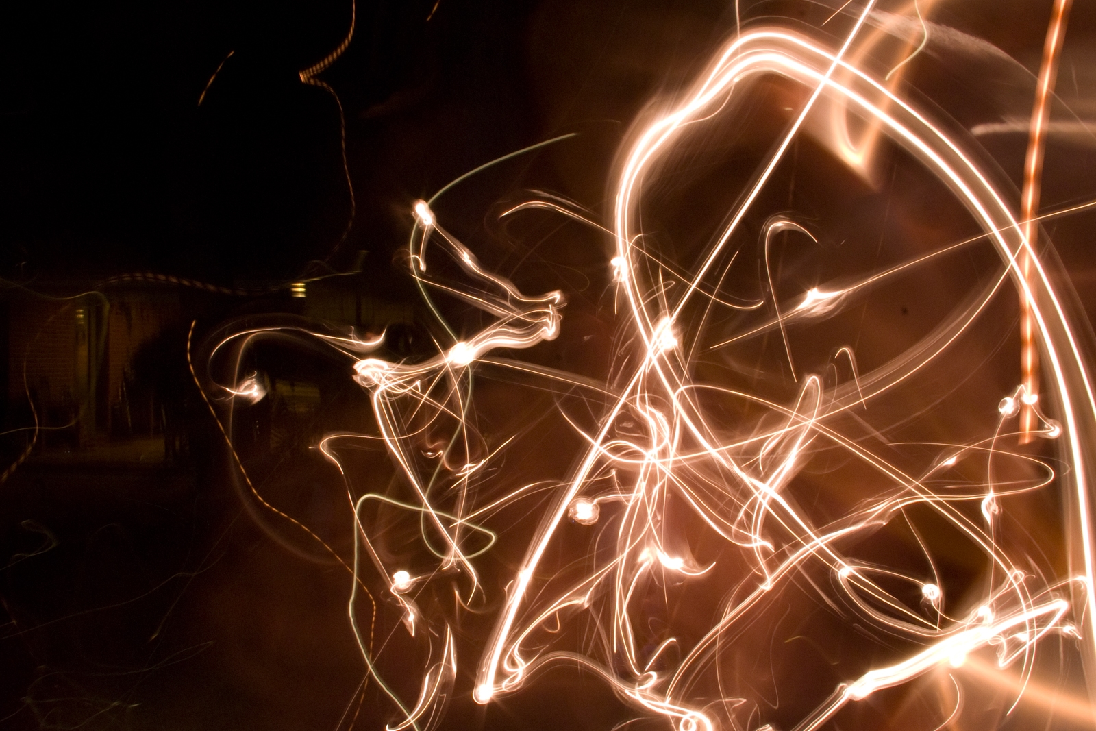 This abstract photograph captures a chaotic array of swirling light trails, likely created through long-exposure photography. The light lines are mostly warm tones, glowing with a mixture of curves, loops, and zigzags that create a sense of motion and energy. The dark background contrasts sharply with the vibrant light patterns, giving the image a dynamic and mesmerizing quality. The streaks of light appear fluid and spontaneous, as if tracing invisible paths through the air. The overall effect is abstract and artistic, evoking a feeling of kinetic energy and movement.
