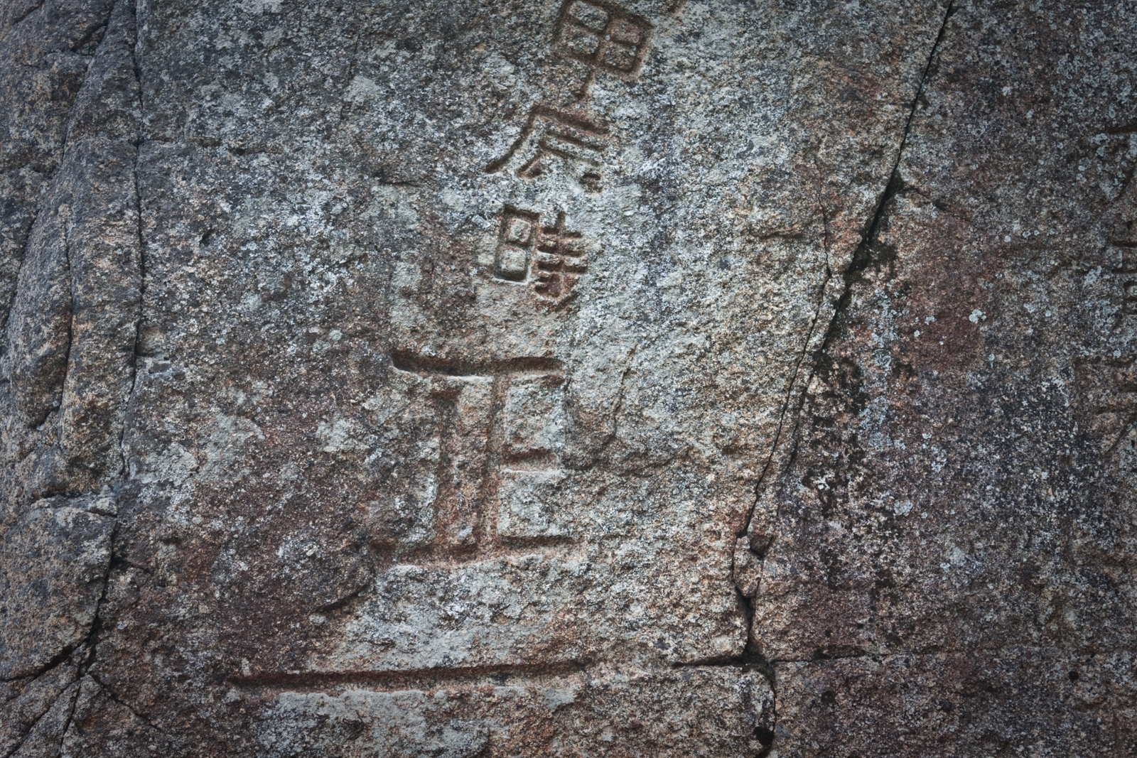 Close-up of characters carved into a large stone, showing detailed ancient writing etched into the rock surface.