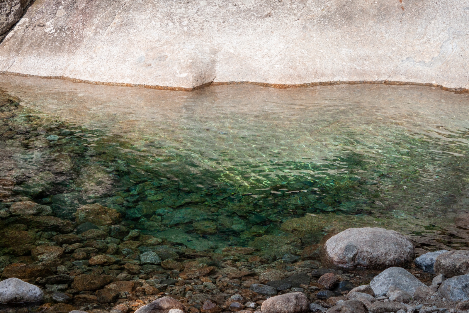 A shallow, clear pool of water, with smooth rocks visible underneath, reflecting the sunlight.
