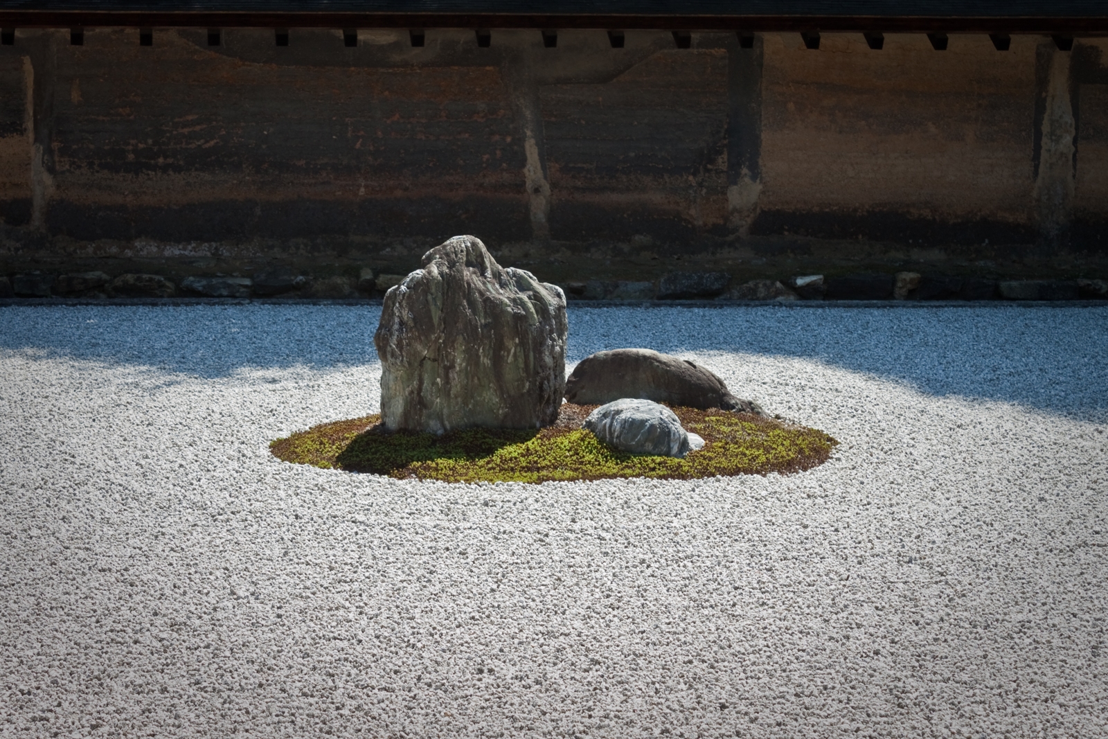 A minimalist Zen rock garden featuring a central arrangement of large stones surrounded by meticulously raked white gravel. The garden exudes simplicity and calm, inviting contemplation and reflection.