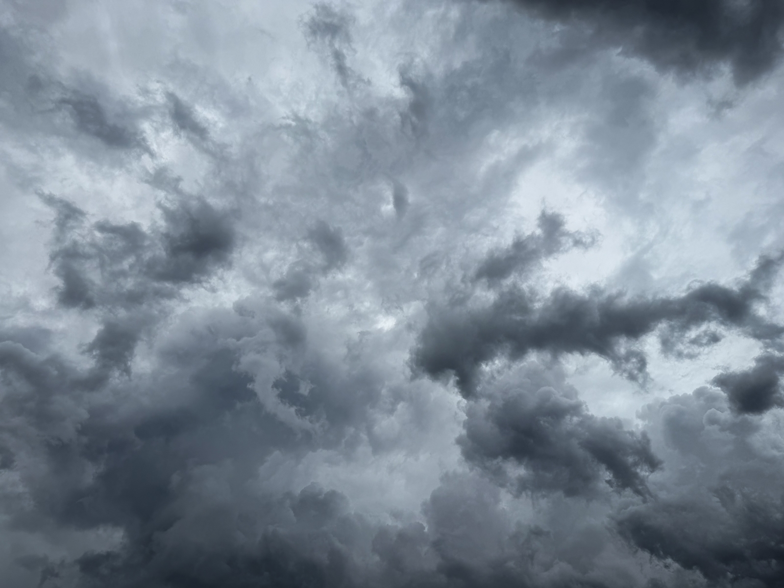 A dramatic, overcast sky filled with turbulent gray storm clouds in varying shades, some dark and heavy, others lighter where the sun filters through.