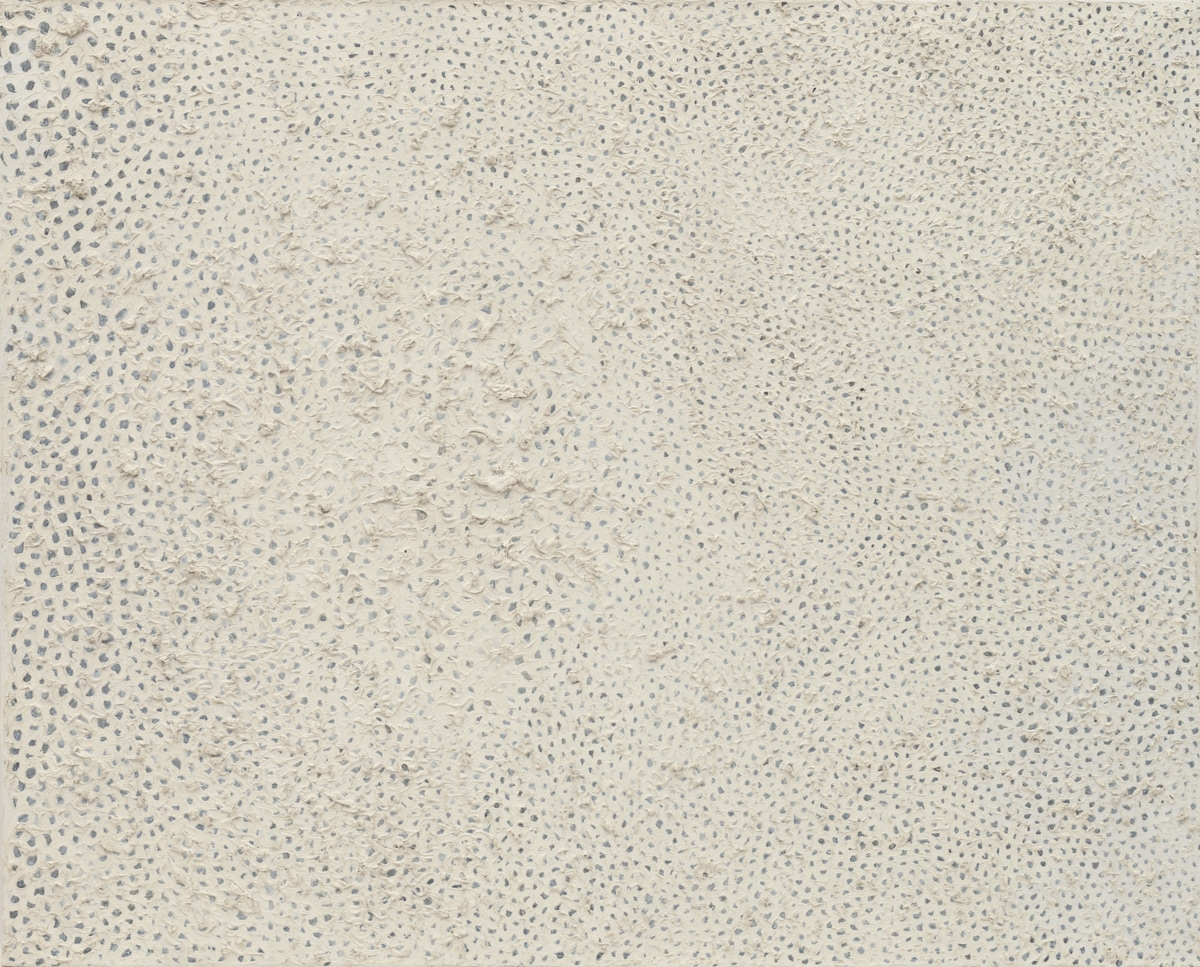 This artwork seems to be a minimalist, textured piece, with small, repetitive patterns creating a tactile surface. The subtle monochromatic palette of whites and grays allows the focus to fall on the material's texture, giving it a quiet, meditative quality.