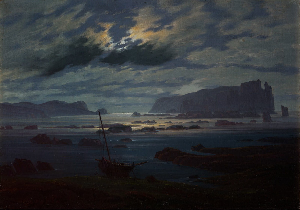 A rugged coastline under a moonlit sky. Waves lap gently under a glowing cloud bank, casting silvery reflections. An abandoned boat lies grounded in the foreground, adding to the stillness.