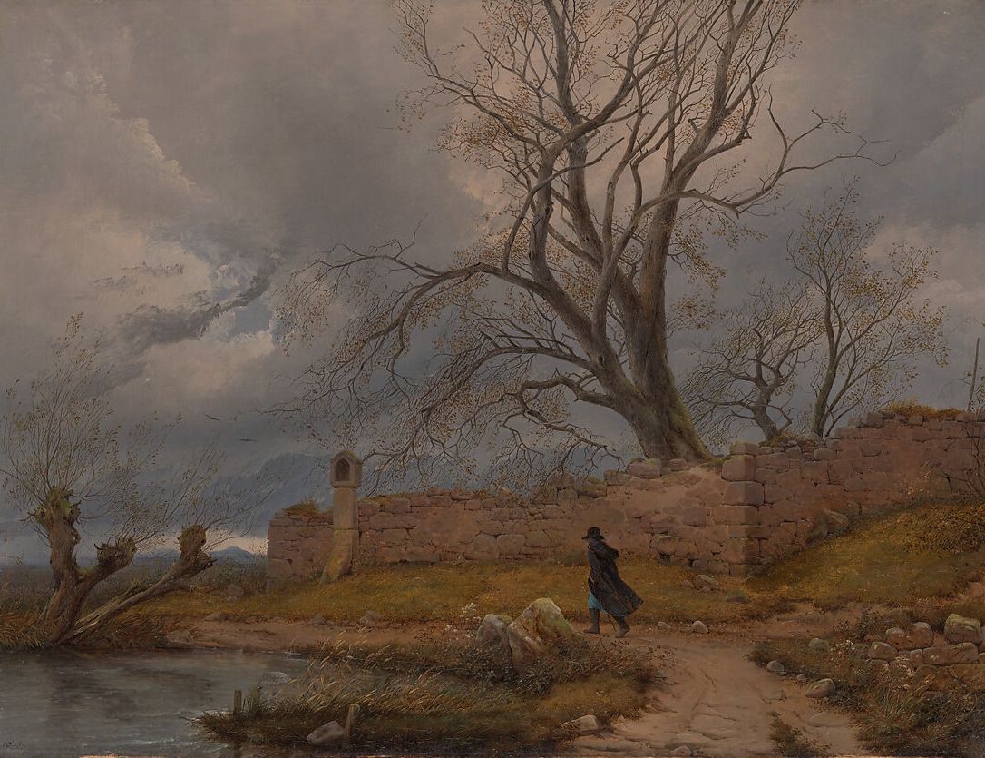 A lone traveler in a dark cloak walks a path beside crumbling stone ruins beneath a massive, leafless tree. The sky is heavy with dark storm clouds, and the landscape exudes a haunting stillness, capturing the sublime tension between man and nature.