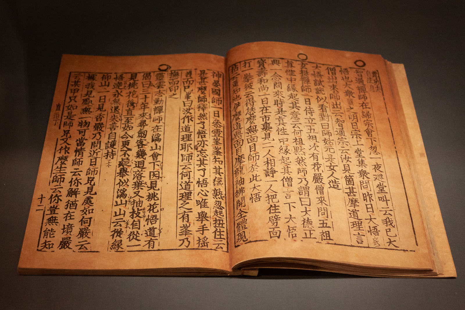A close-up shot of an open ancient manuscript written in an East Asian script, featuring vertical lines of characters on aged, yellowed paper. The text is neatly aligned, giving an impression of careful preservation.