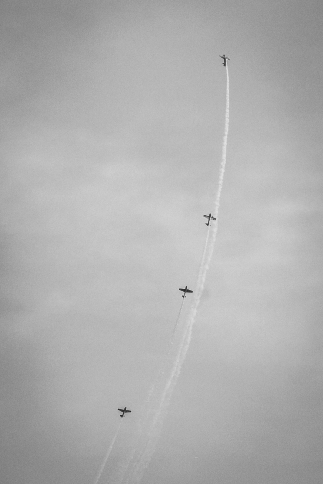 Four airplanes ascending vertically in a staggered line, leaving smoke trails behind them, in a black-and-white image.