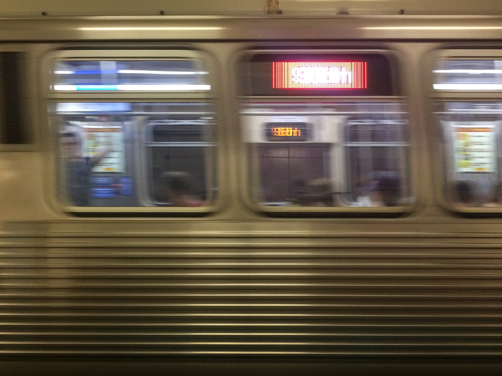 Blurred image of a subway train in motion, with a digital display reading the destination and passengers faintly visible through the windows as the train speeds by.