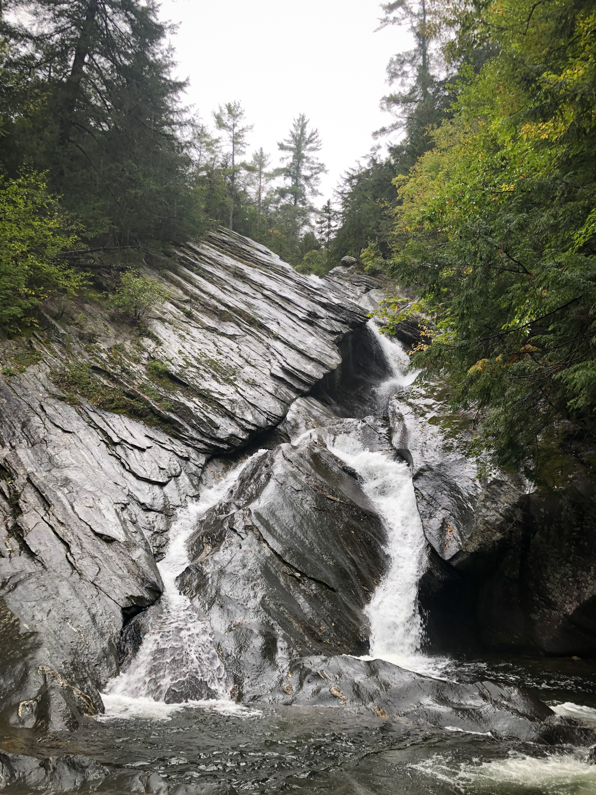 A cascading waterfall flowing down large, angled rock formations in a forest.
