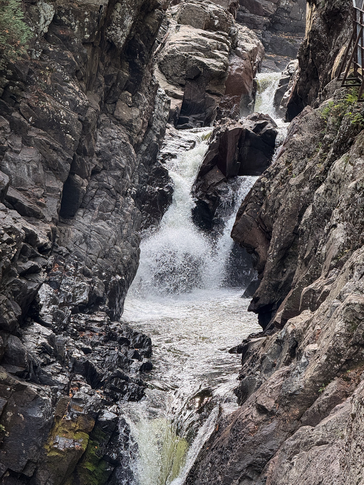 Water cascading through a steep, rocky gorge, foaming white as it tumbles over jagged dark stone.